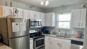 A modern kitchen with white cabinets, stainless steel appliances, a granite countertop, and a window providing natural light. - Sunrise Village #216 by Southern Vacation Rentals (Gulf Shores)