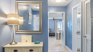 A hallway with a mirror, a lamp, a framed sign, and a door leading to another room. - Grand Beach Resort by Southern Vacation Rentals (Gulf Shores)