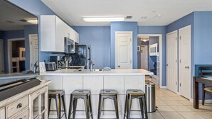 A modern kitchen with a central island, bar stools, stainless steel appliances, and blue walls. - Grand Beach Resort by Southern Vacation Rentals (Gulf Shores)