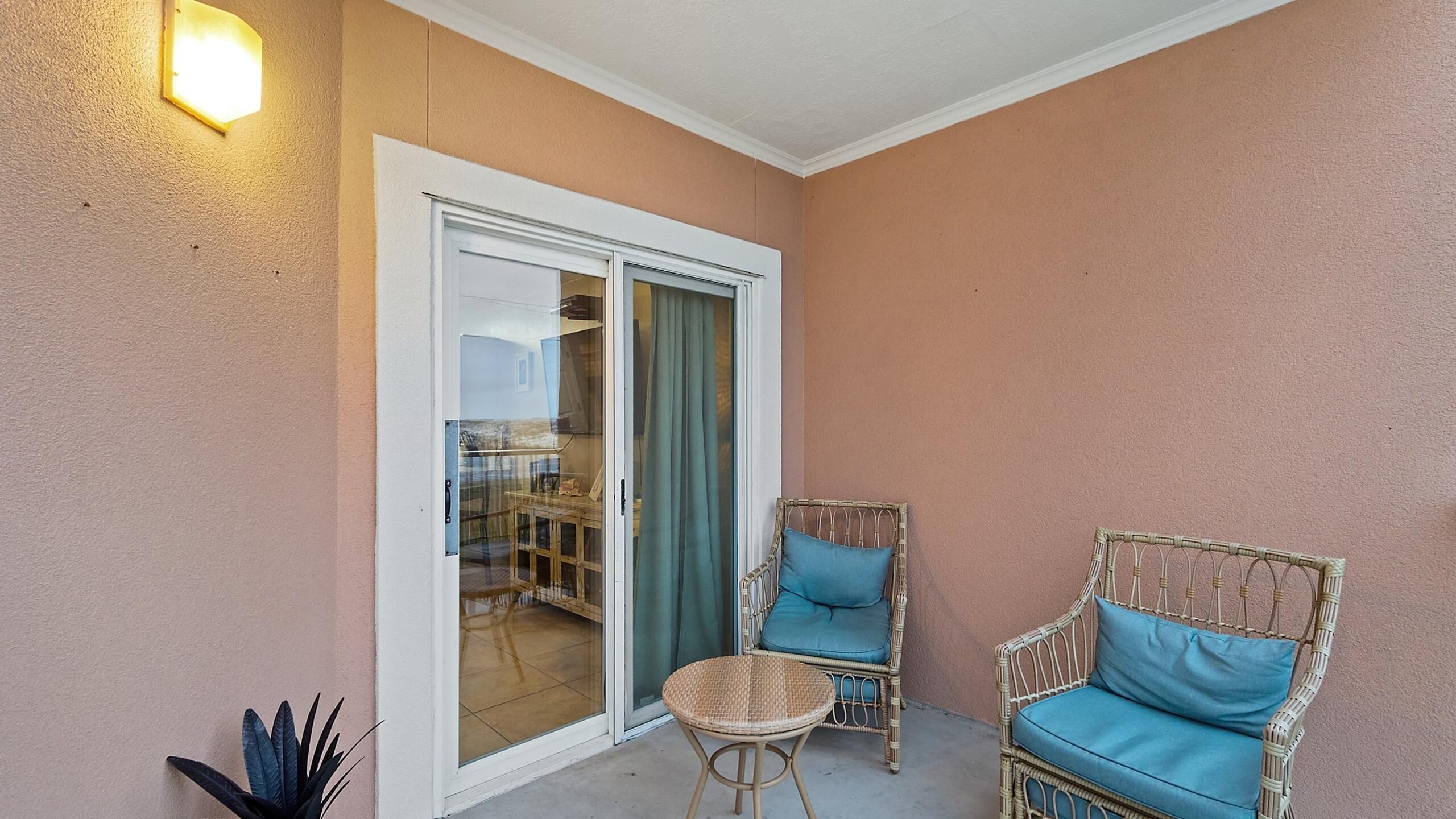 A balcony with wicker furniture, a sliding glass door, and a wall-mounted light fixture.