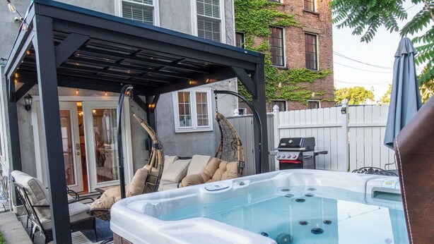 Un bain à remous situé sous un patio couvert, avec un espace salon et un barbecue.