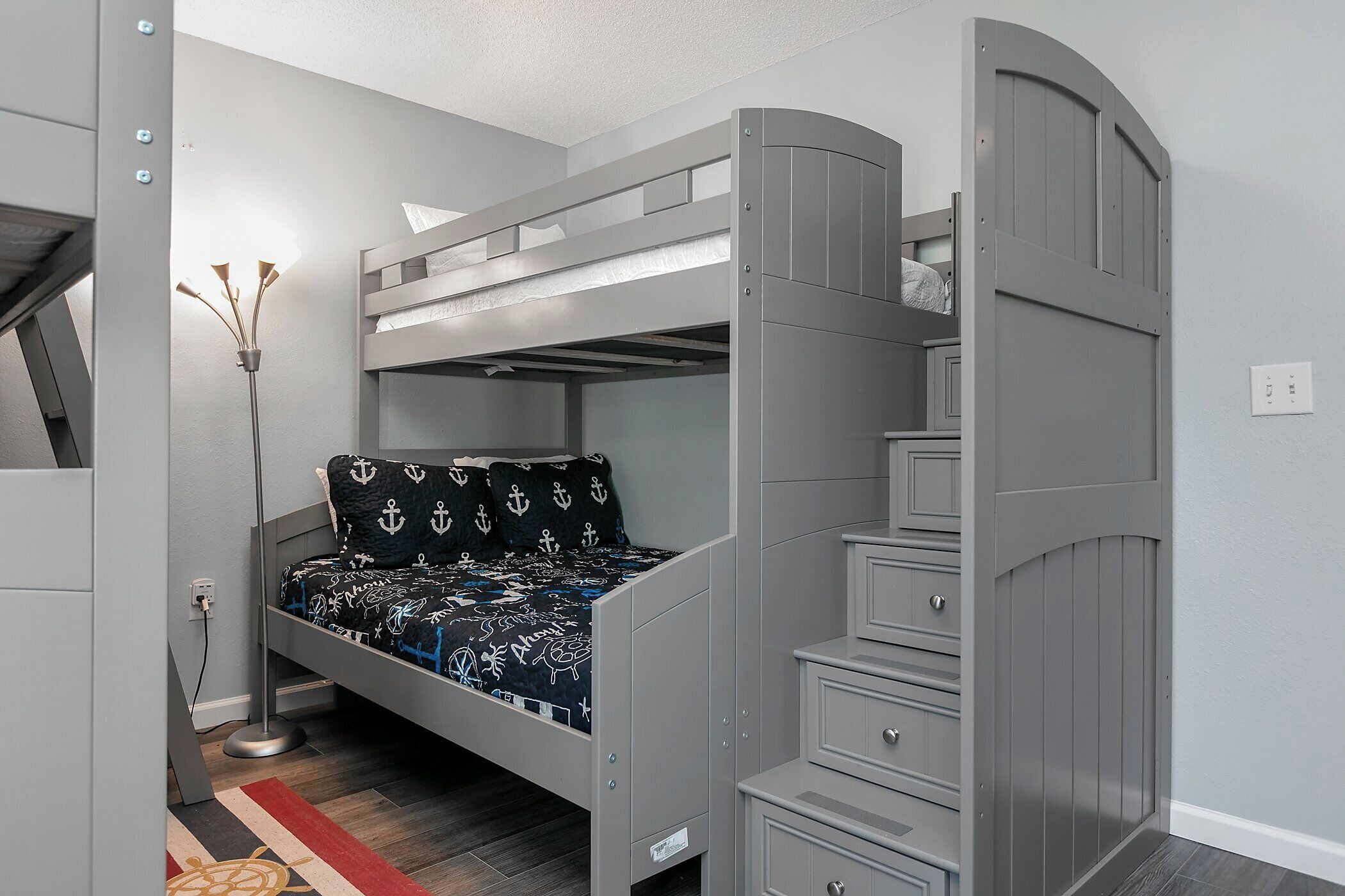 Ein Etagenbett mit Schreibtisch und Schubladen, eine Stehlampe und eine deckenbedeckende Tagesdecke mit Muster.