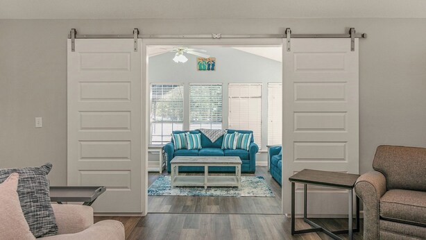An open sliding door leading to a living room with a blue sofa, a coffee table, and a gray armchair. - Happy Ours by Southern Vacation Rentals (Foley)