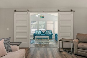 Una porta scorrevole aperta che dà su un soggiorno con un divano blu, un tavolino da caffè e una poltrona grigia.