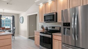 A modern kitchen with stainless steel appliances, wooden cabinets, and a tiled floor. - Happy Ours by Southern Vacation Rentals (Foley)