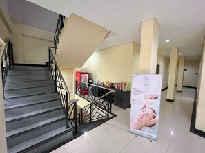 A hotel lobby with a staircase, a vending machine, and a spa service poster. - Tentrem BS Residence (Semarang)