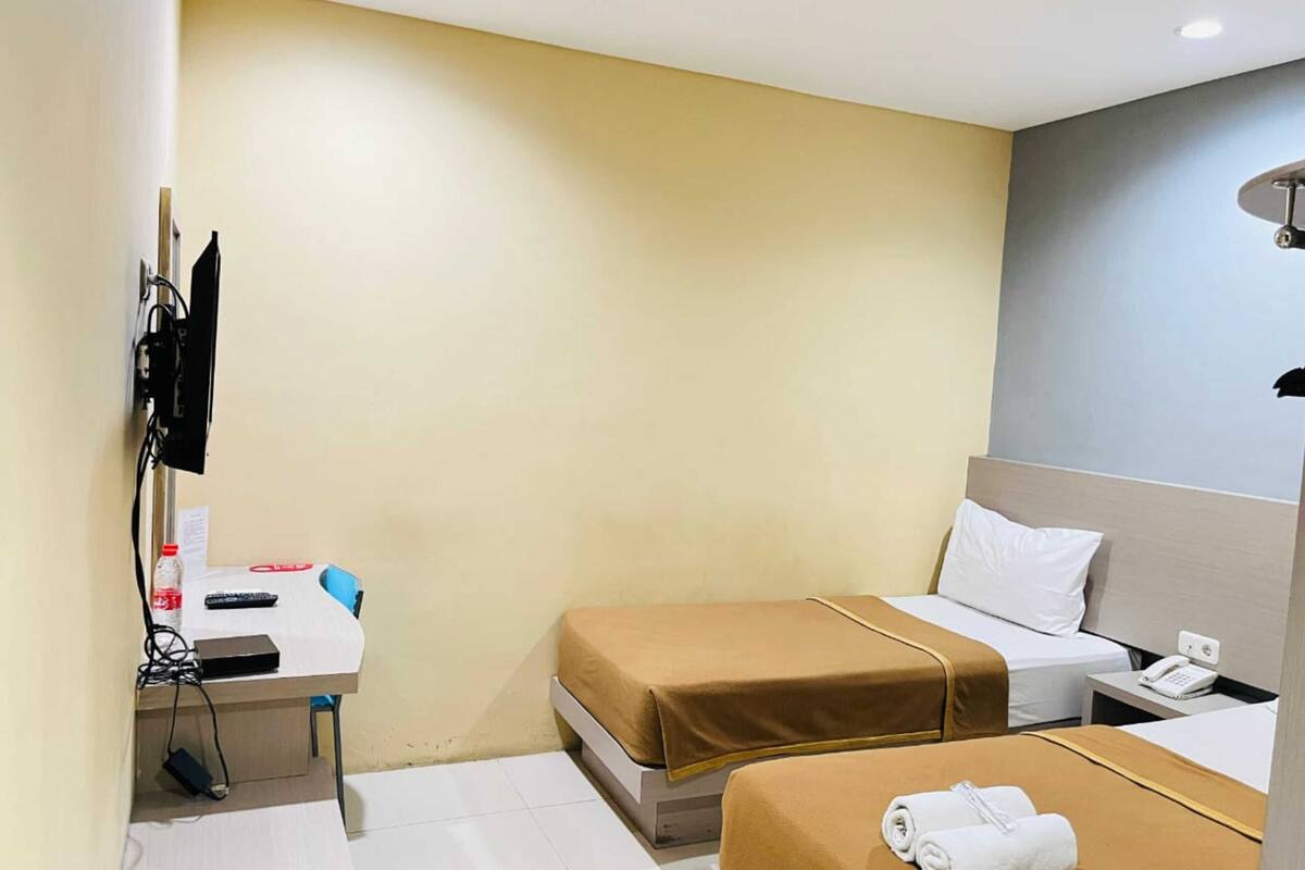A hotel room with two beds, a desk, a chair, a telephone, and a wall-mounted TV.
