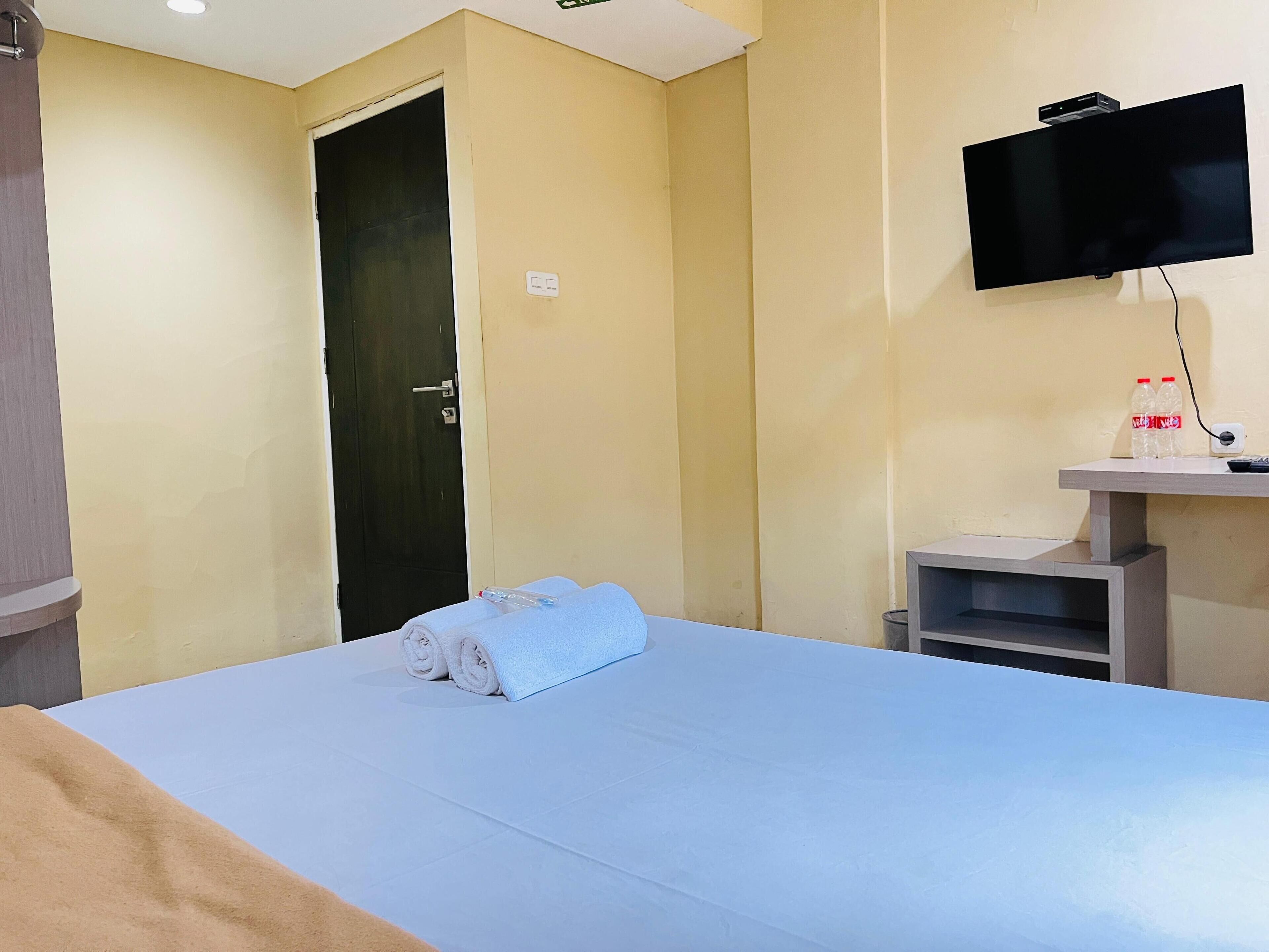 A hotel room with a bed, a television mounted on the wall, a door, and a small table with a bottle and remote control.