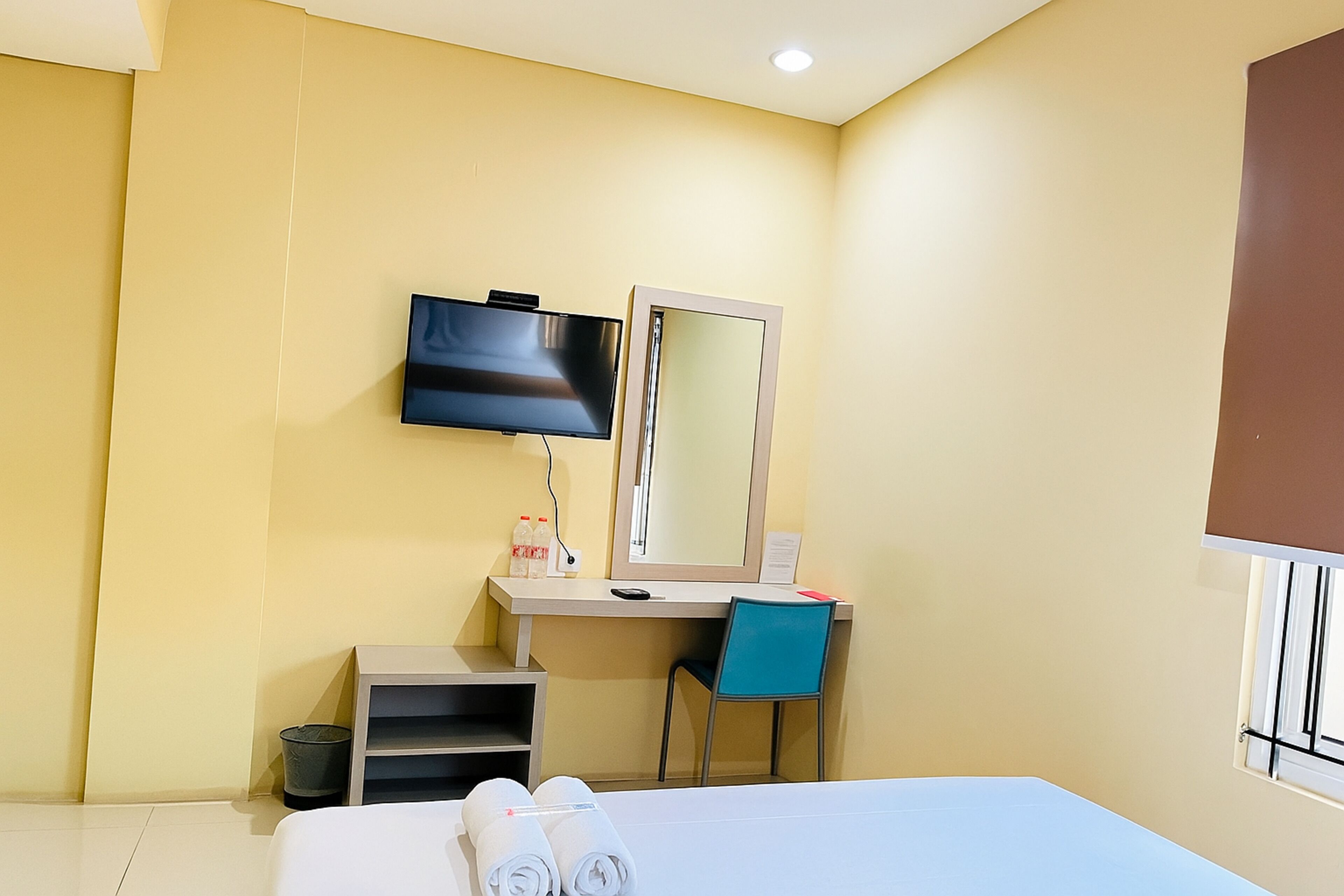 Una habitación de hotel con una cama, un escritorio con una silla, un televisor y un espejo.