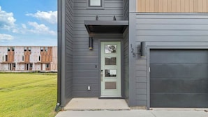 A modern two-story house with a light green front door, a garage door, and a small porch area with a light fixture.