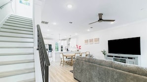 A modern living room with a grey sofa, a flat-screen TV, and a dining area with wooden furniture.