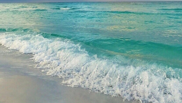 A beach with turquoise water and waves crashing onto the shore.