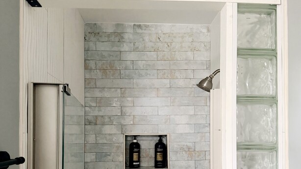 Ducha con pared de piedra, puerta de cristal y dos botellas de champú en la pared.