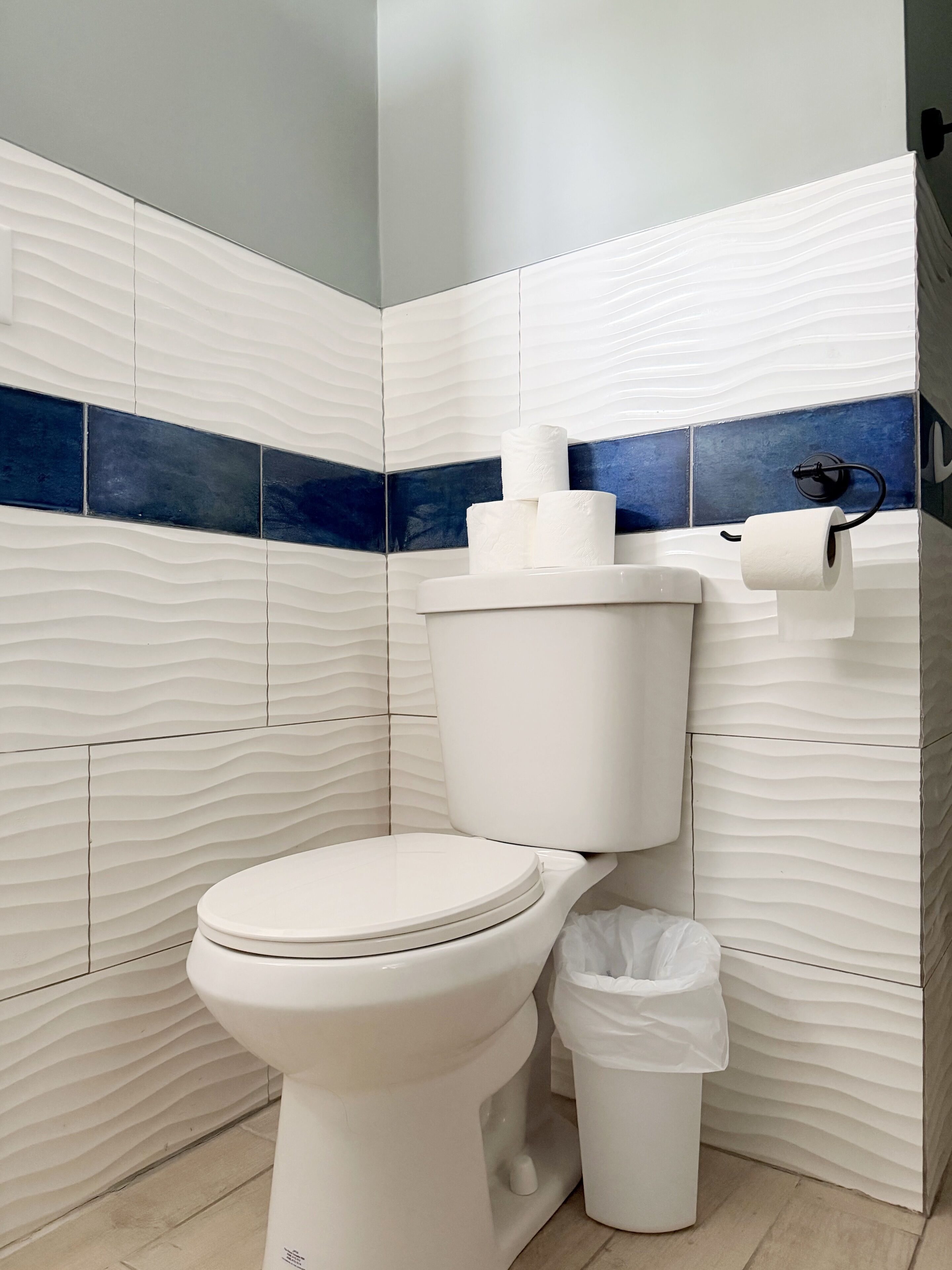 Un baño moderno con un inodoro blanco, un cubo de basura y un dispensador de papel higiénico en la pared.