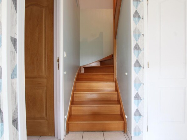 Un escalier en bois mène à une pièce dotée d’une porte blanche et d’un mur orné de motifs.