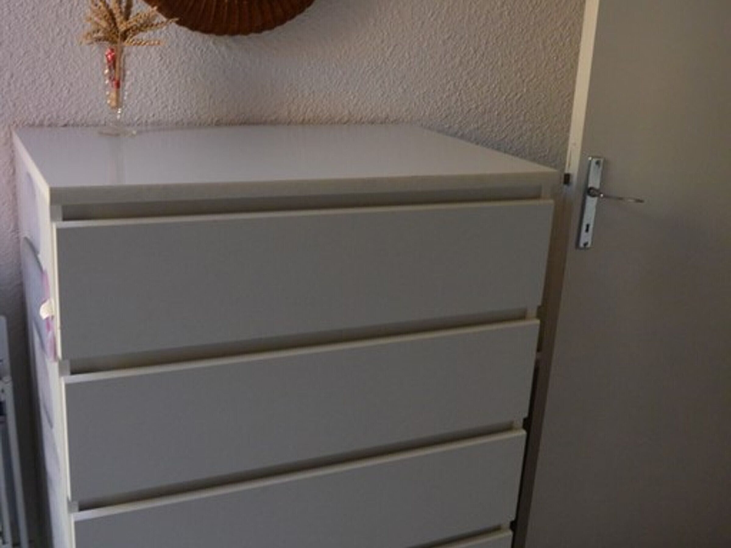 A white cabinet with four drawers against a textured wall.