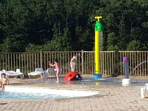 A swimming pool area with a water play structure, lounge chairs, and a wooden fence.