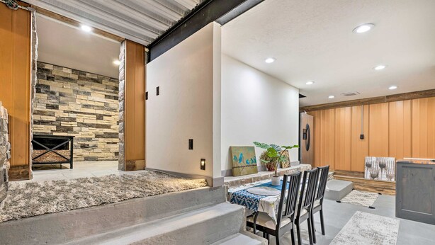 A modern interior with a stone wall, a dining area with chairs and a table, and a staircase leading to an outdoor area.