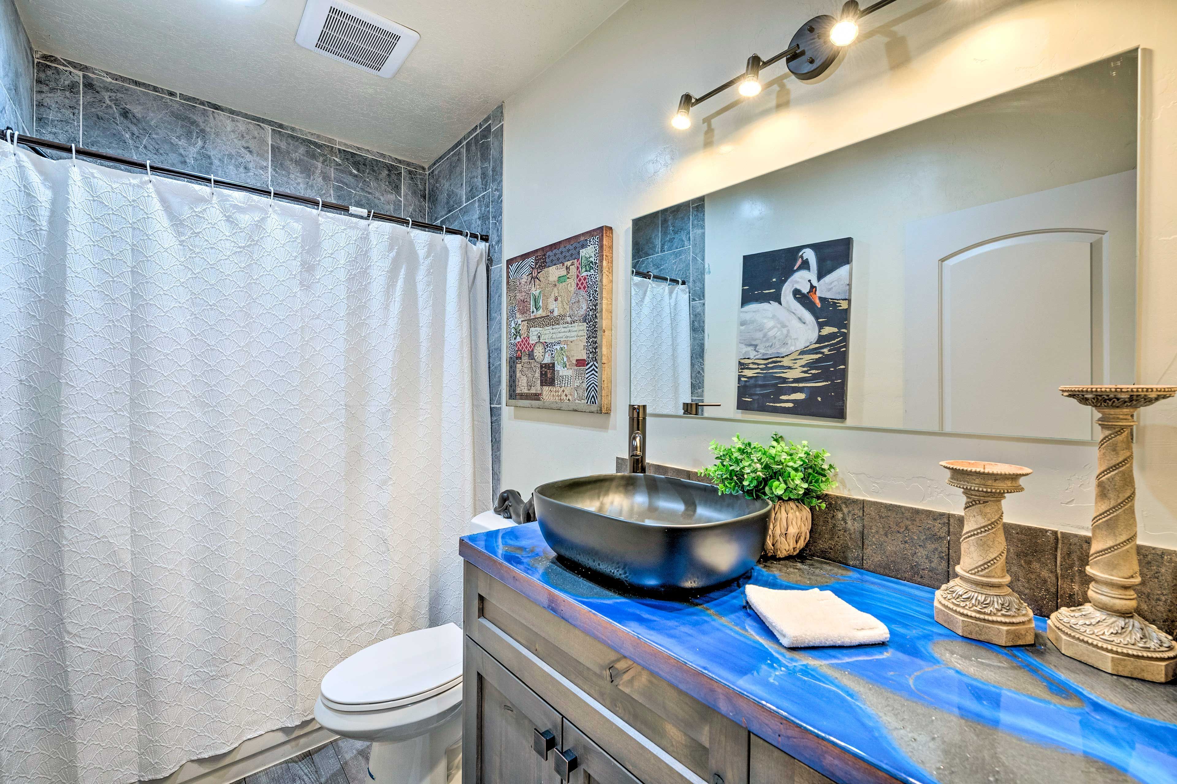 A bathroom with a large bathtub, a sink with a decorative bowl, and a mirror with artwork.