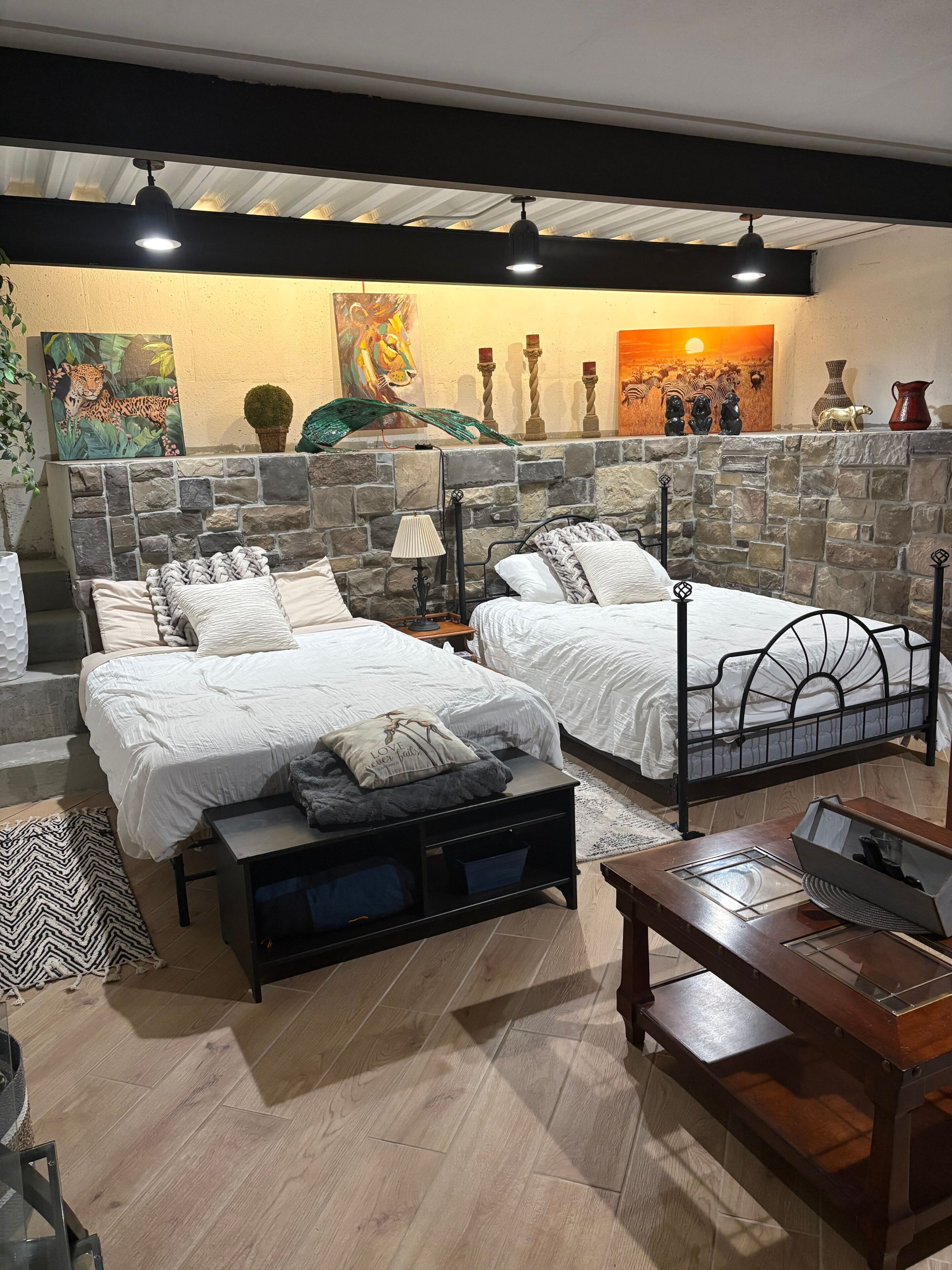 Une chambre avec deux lits, un mur en pierre, des œuvres d’art et une cheminée.