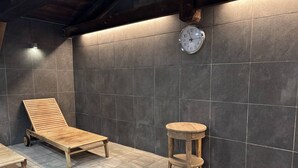 Una habitación iluminada por el sol con una silla de madera, una mesita redonda y un reloj en la pared.