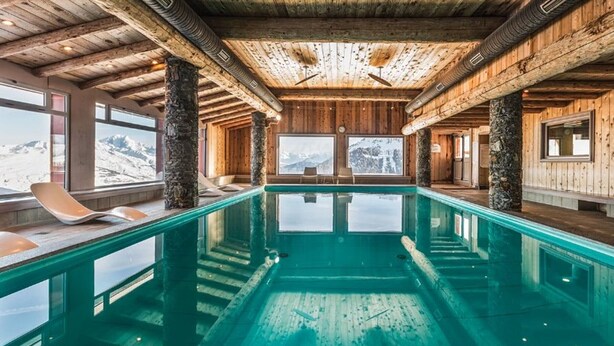 Una amplia piscina interior con paredes de madera y vistas a montañas nevadas.