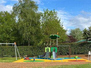 A playground with slides and swings, surrounded by trees and a hedge. - Cozy mobile home with terrace at Naucelle campsite (Naucelle)