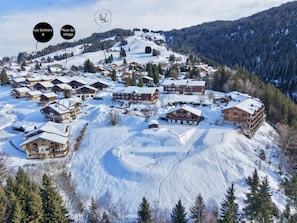 Un pueblo cubierto de nieve en la montaña, con chalets de madera y una pista de esquí.