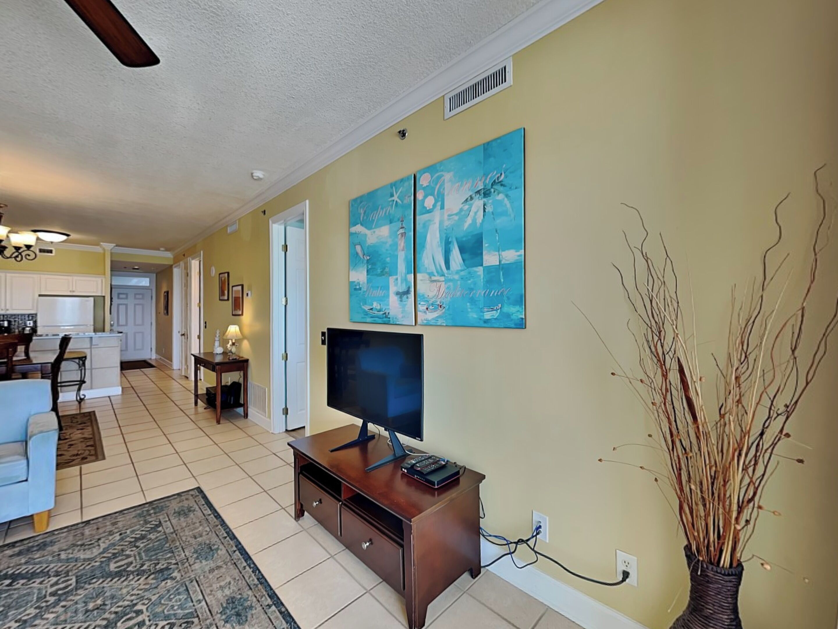A living room with a TV, a dining area, and a kitchen in the background.