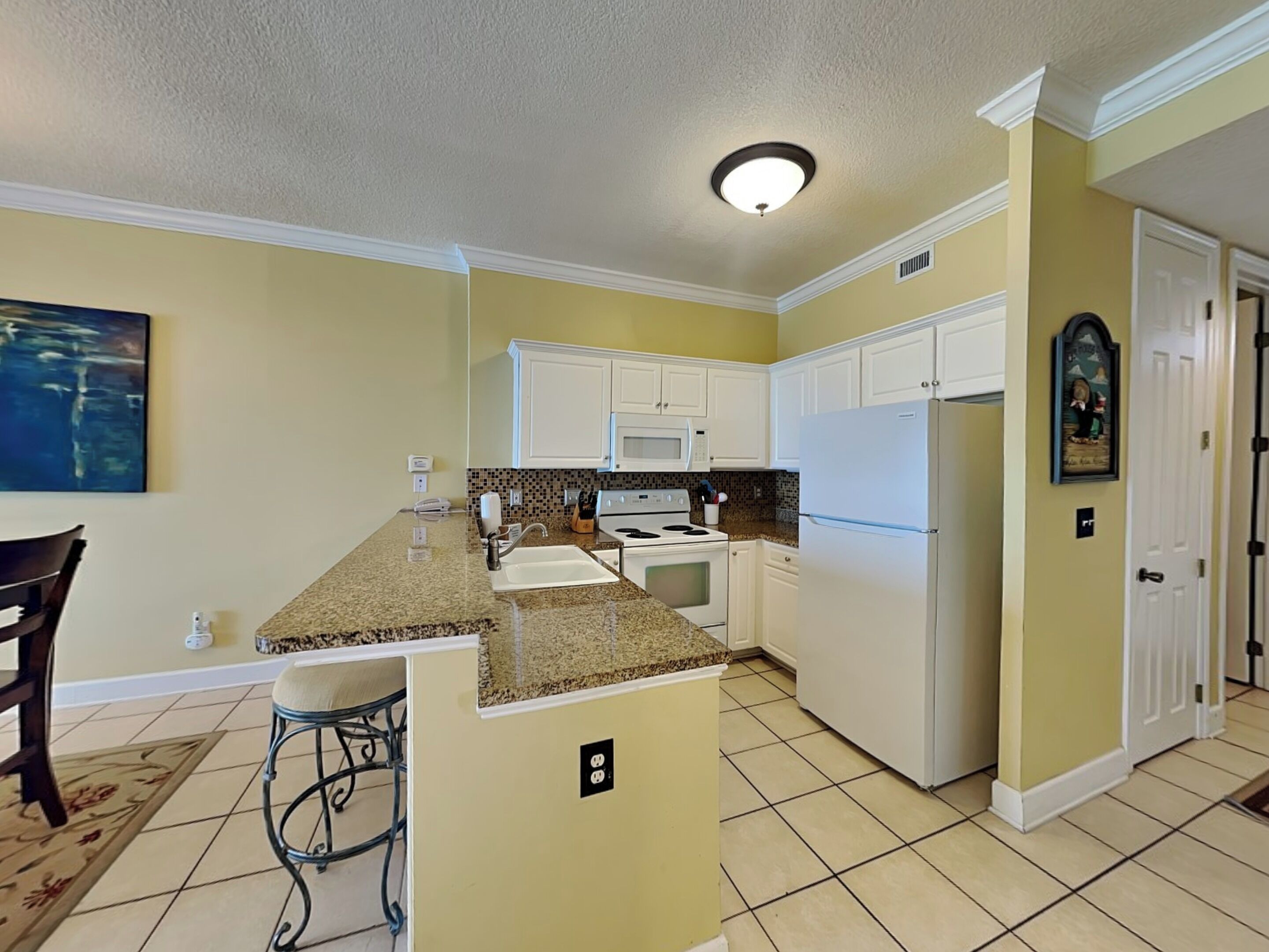 A kitchen with white cabinets, a granite countertop, a microwave, a stove, and a refrigerator.