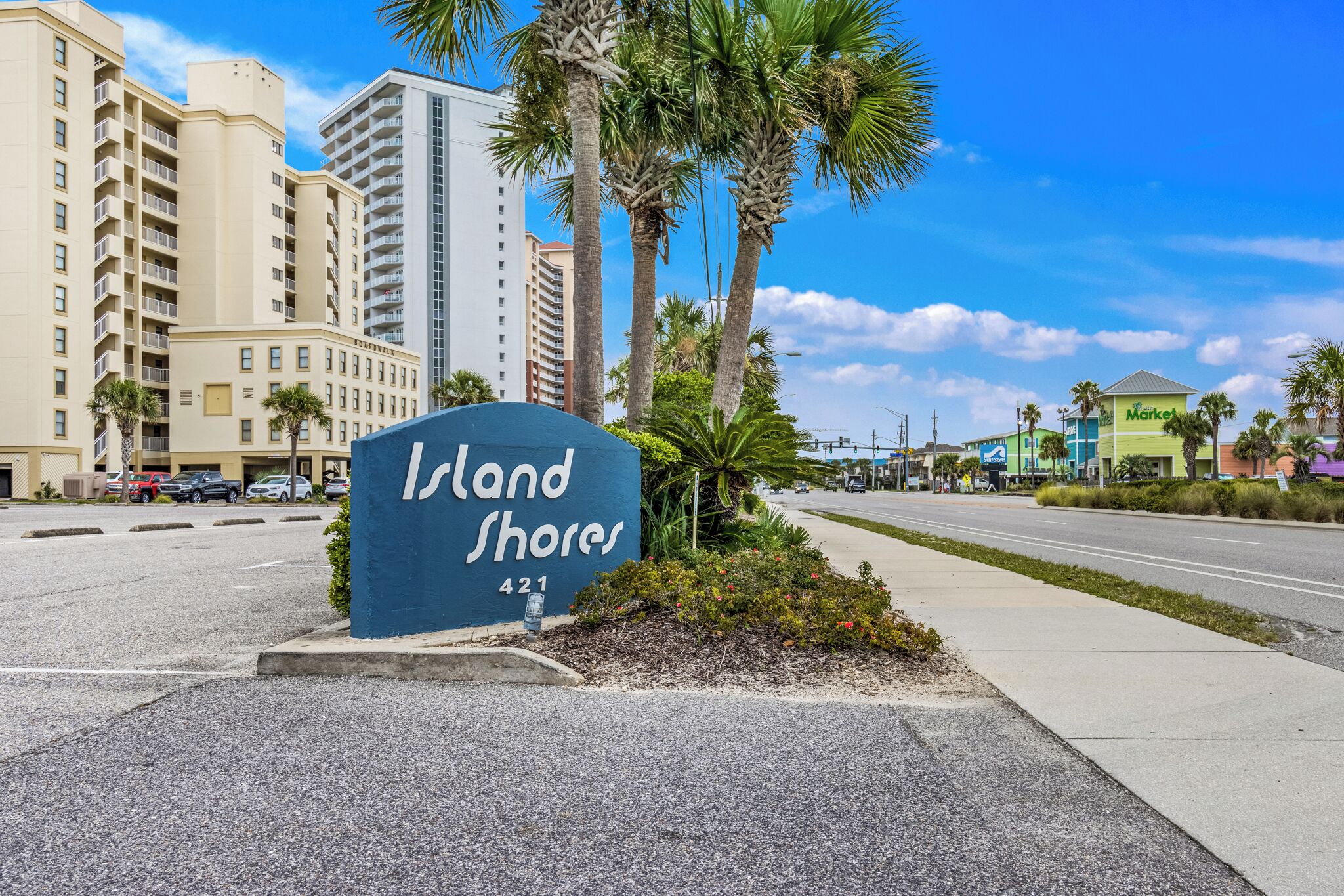 A sign for Island Shores hotel with a clear view of the surrounding buildings and palm trees.