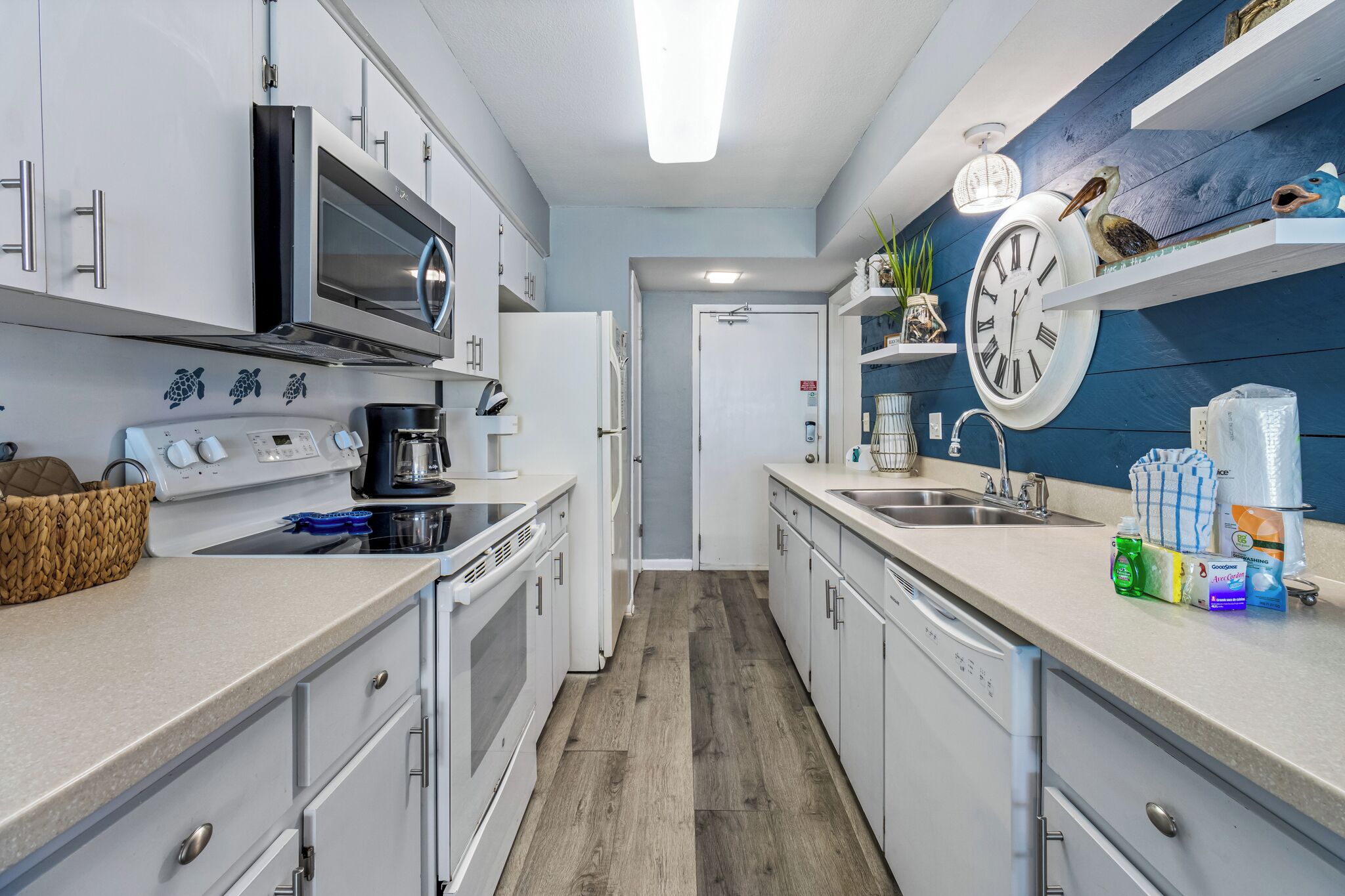 A modern kitchen with white cabinets, stainless steel appliances, and a wooden floor.