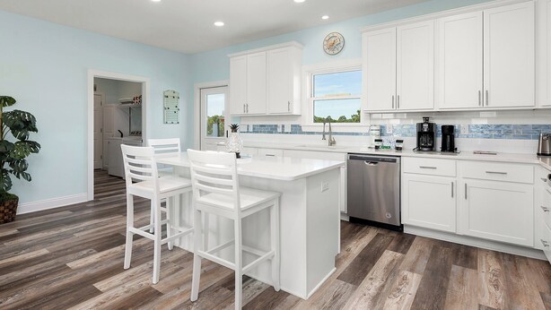 A modern kitchen with white cabinetry, a central island with seating, and a view through the window. - Living The Dream by Southern Vacation Rentals (Gulf Shores)