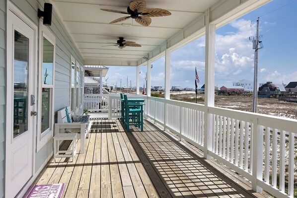 A covered wooden deck with white railings, ceiling fans, and outdoor seating.