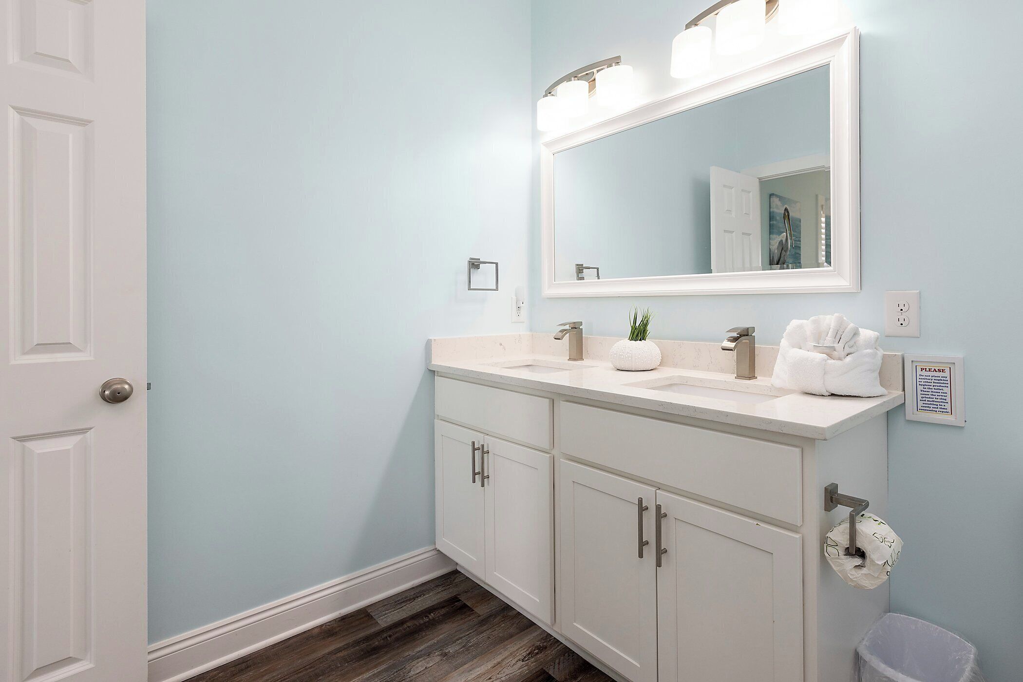 A bathroom with a light blue wall, white vanity, and a large mirror.