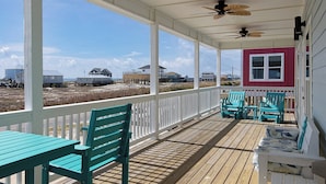 A covered porch with wooden flooring, teal chairs, and a white table. - Living The Dream by Southern Vacation Rentals (Gulf Shores)