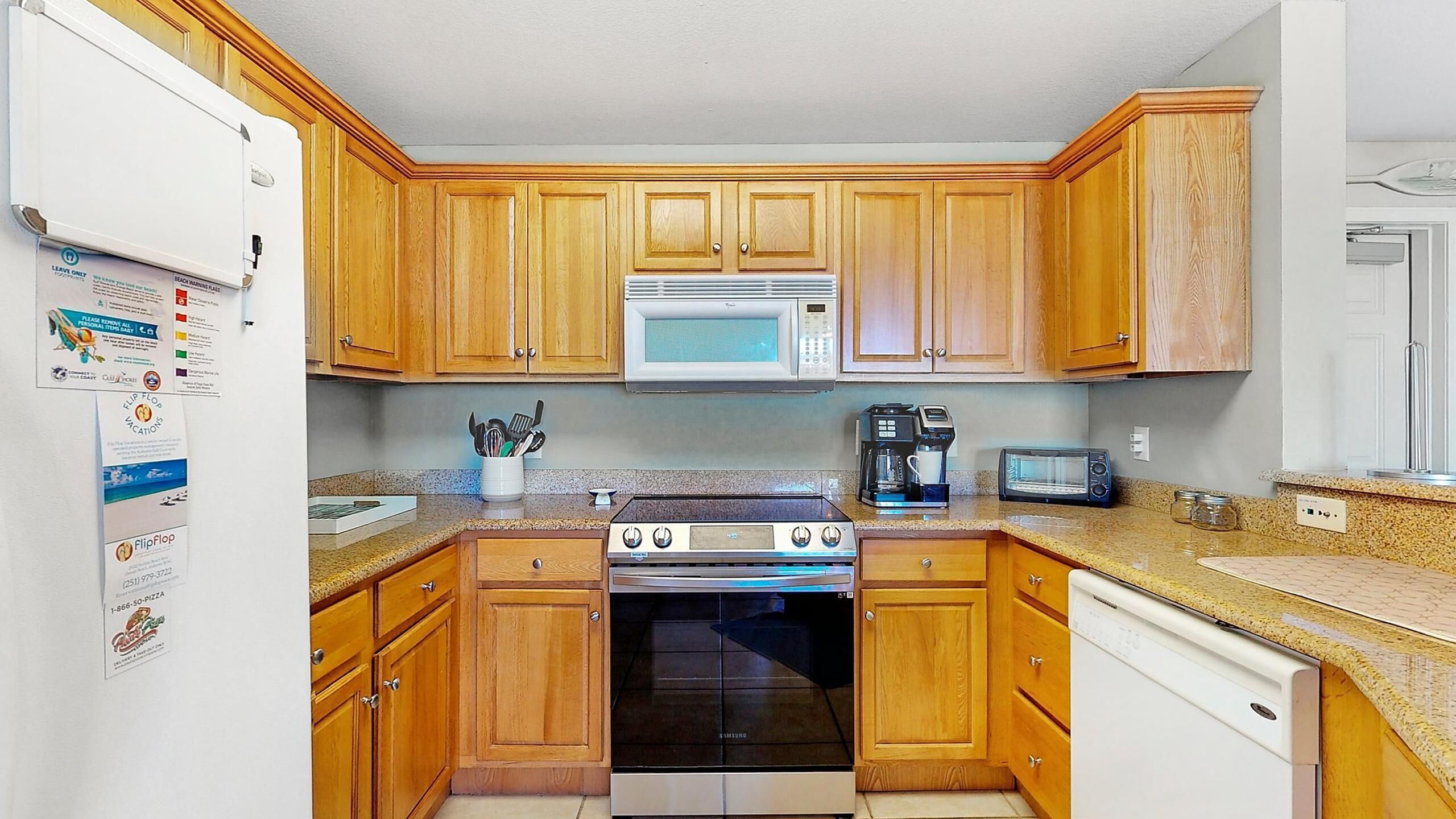 A compact kitchen with wooden cabinets, a microwave, a stove, a dishwasher, and a toaster.