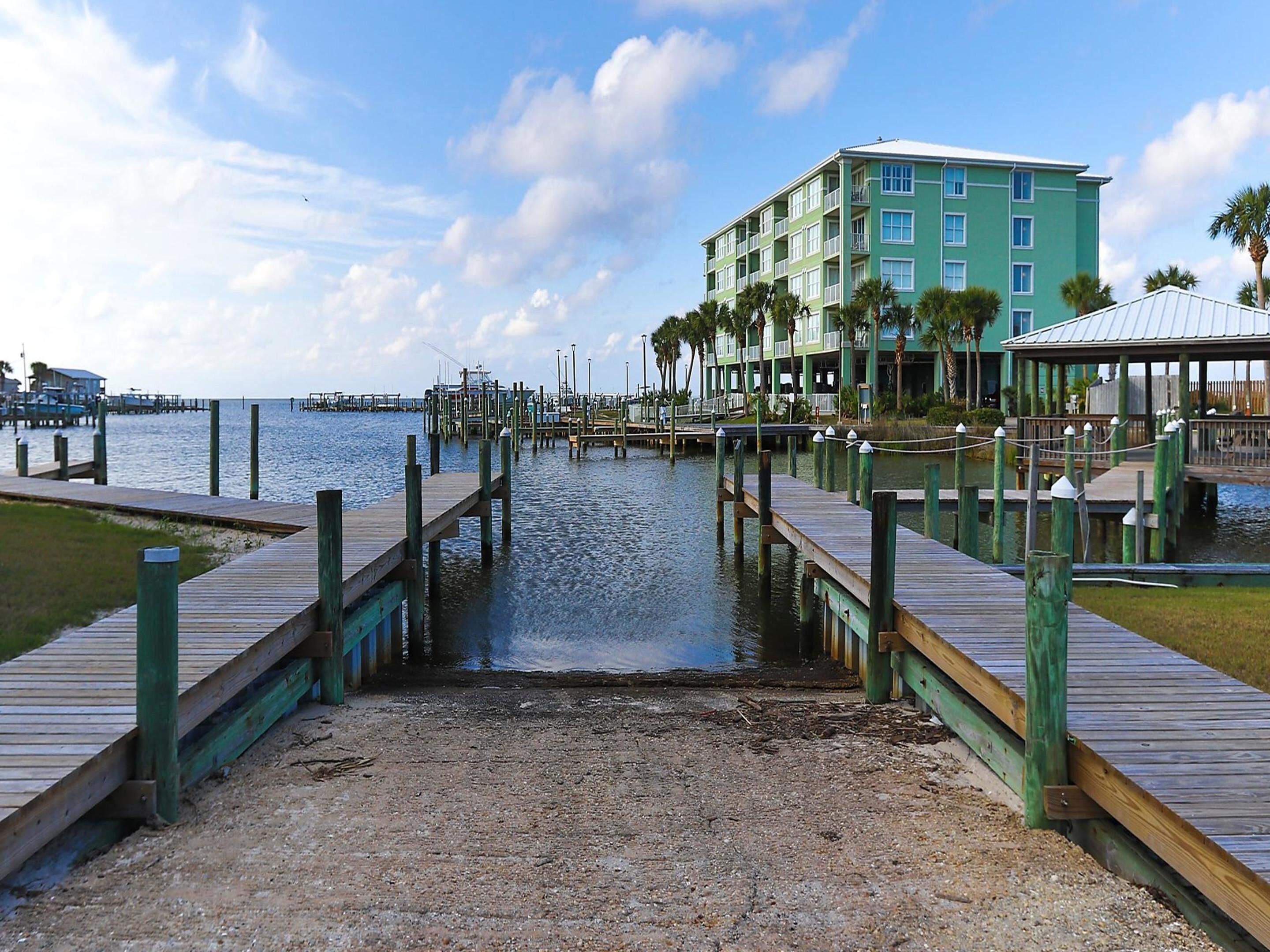 A waterfront hotel with a dock leading to the water, surrounded by palm trees and a clear sky.