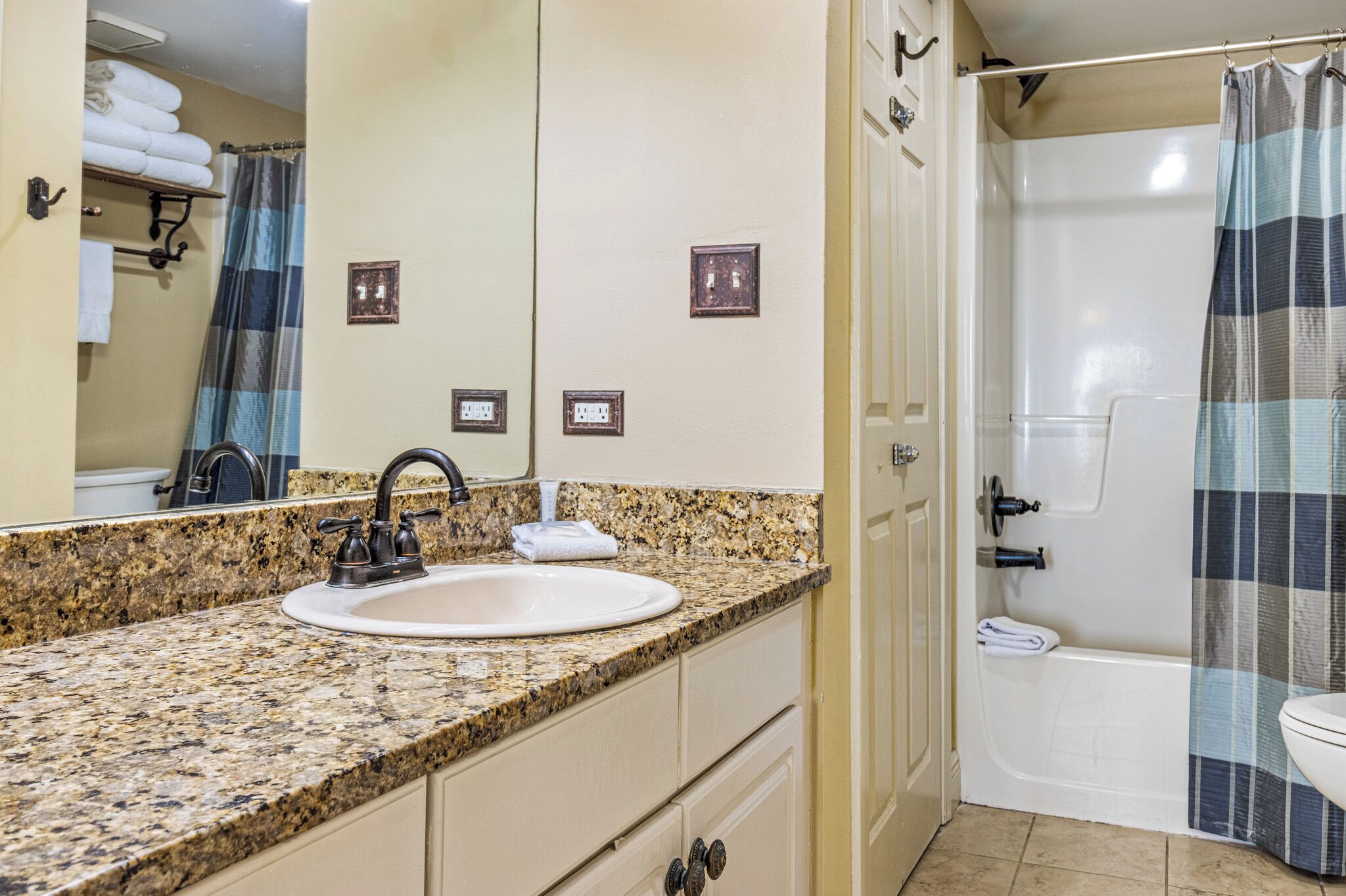 A bathroom with a granite countertop sink, a mirror, a shower with a striped curtain, and a bathtub.