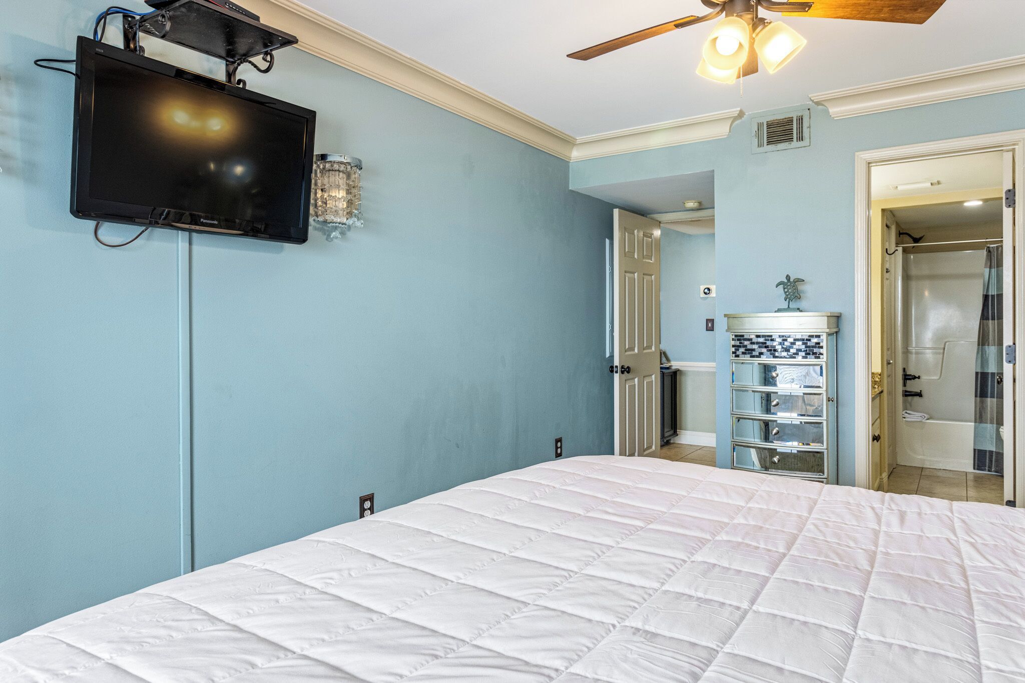 A bedroom with a bed, a mounted TV, and a ceiling fan.