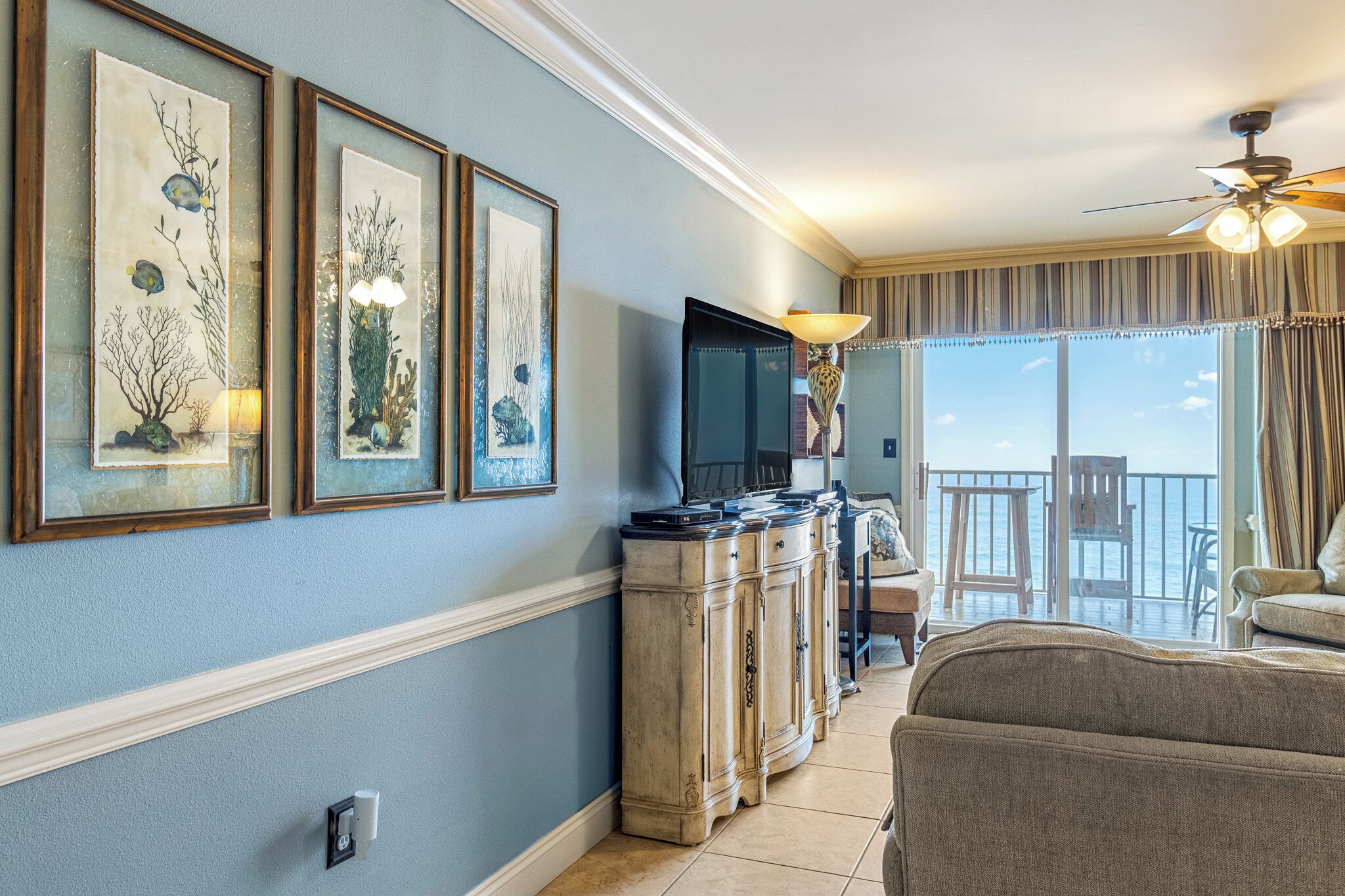 A living room with a TV, framed artwork, a lamp, and a view of the ocean.