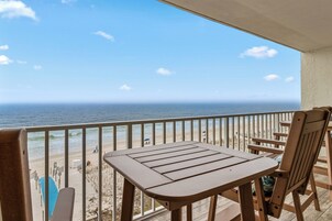 A balcony with a view of the ocean, wooden furniture, and a clear sky.