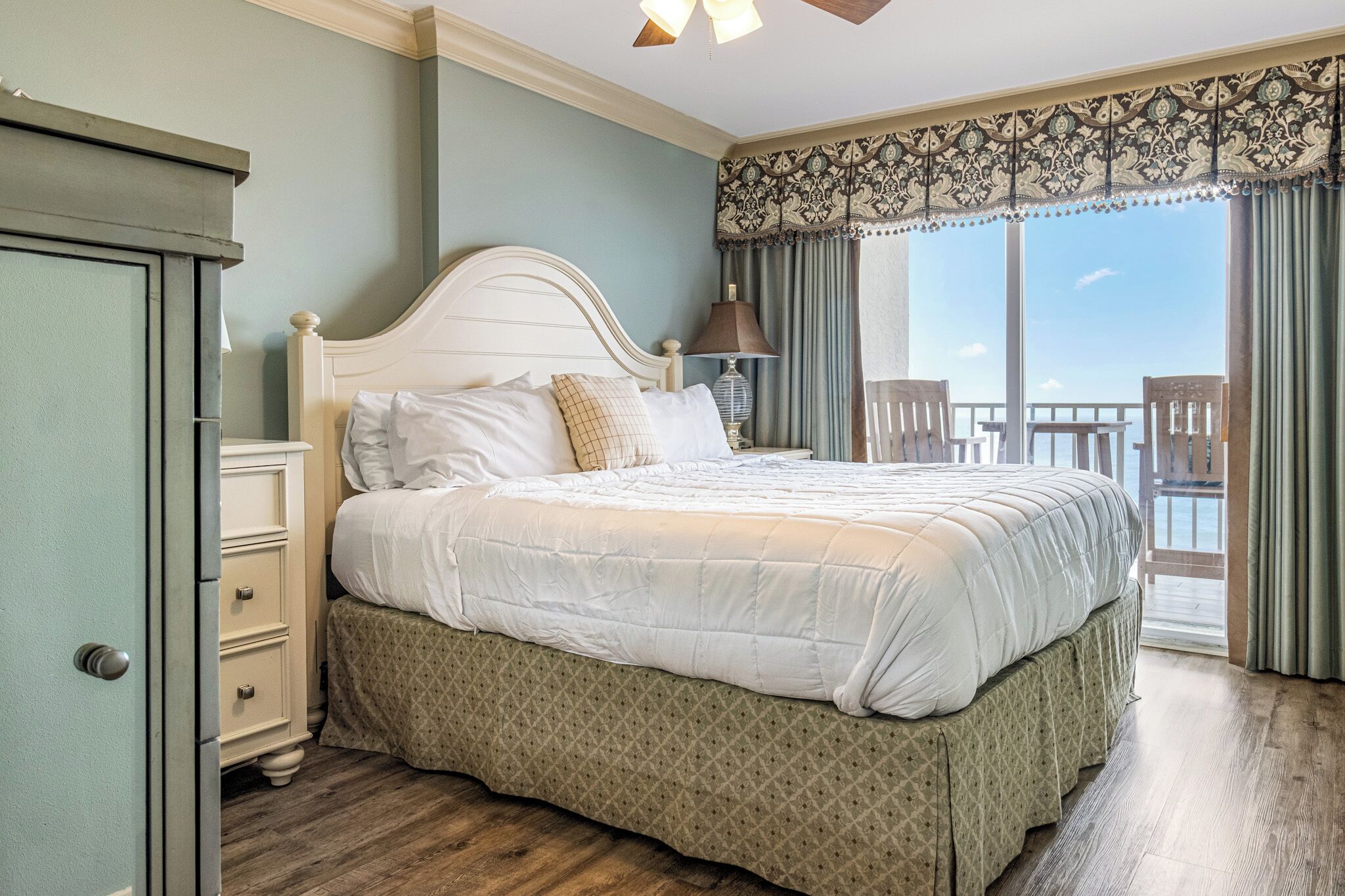 A bedroom with a large bed, a dresser, a nightstand, and a view of the balcony.