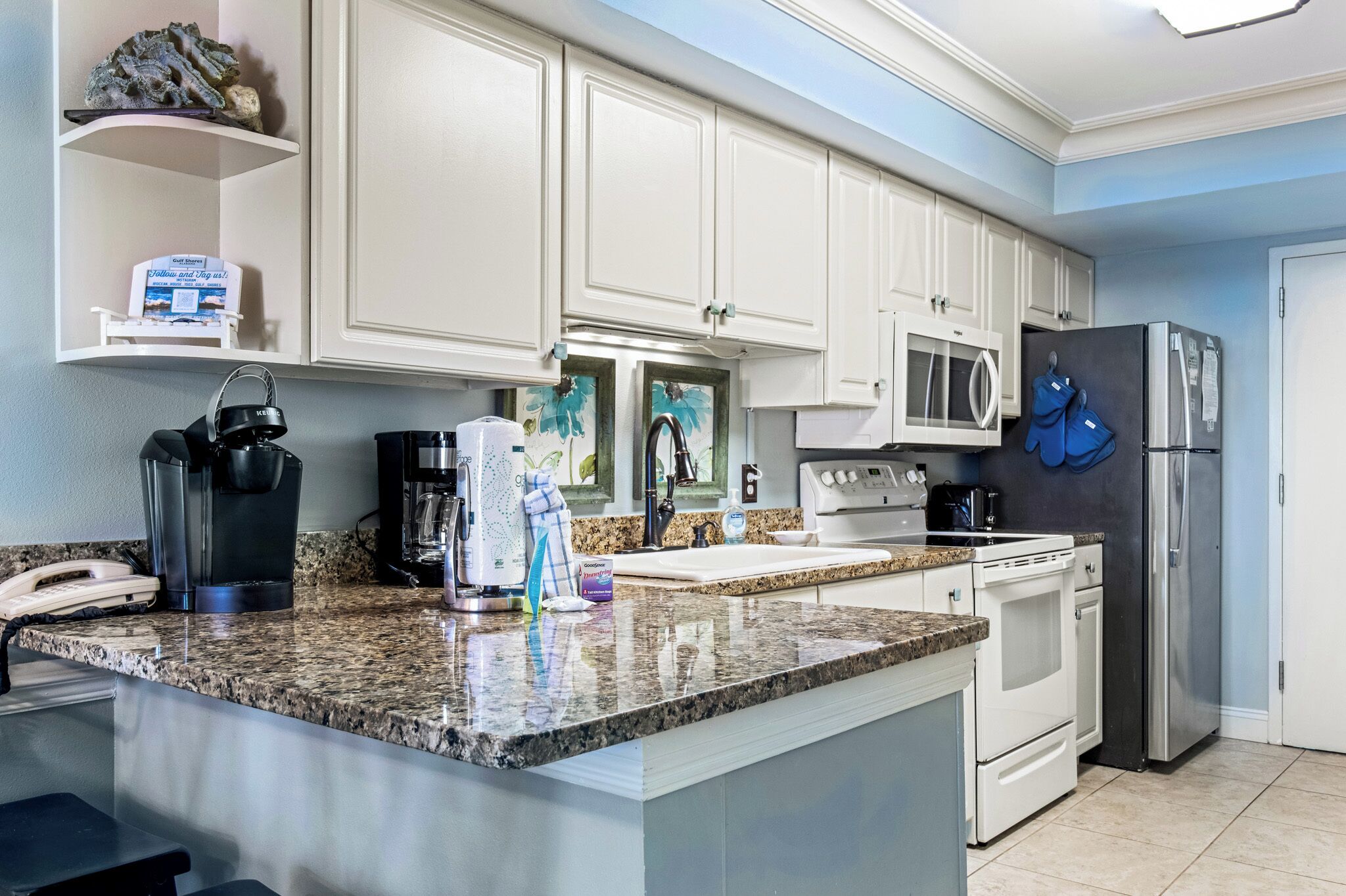 A modern kitchen with white cabinets, granite countertops, a stainless steel refrigerator, and a microwave.