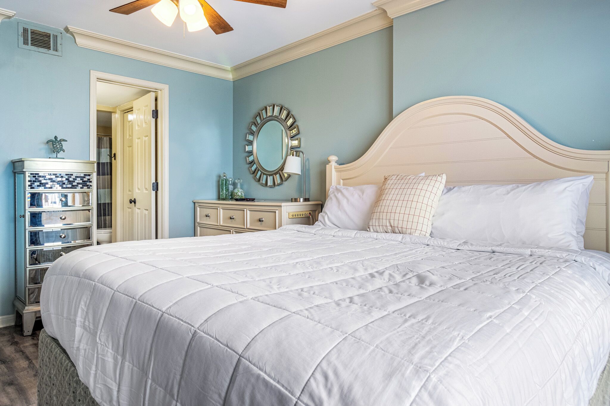 A bedroom with a large bed, a dresser, a mirror, and a door leading to another room.