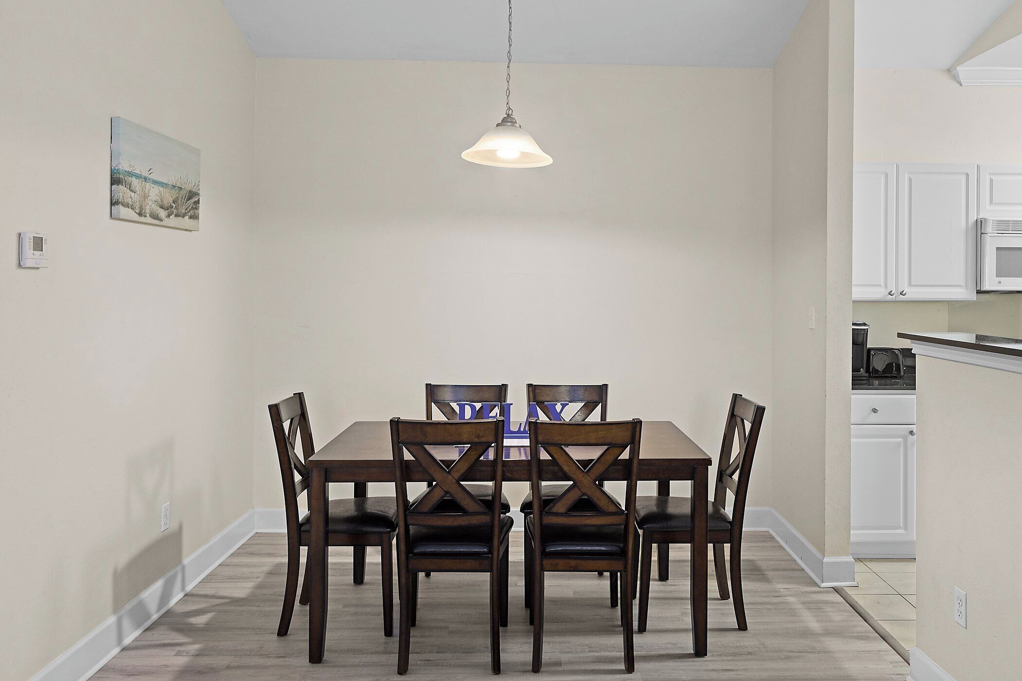 A dining area with a wooden table and chairs, a pendant light, and a kitchen in the background.