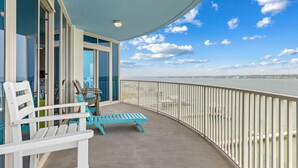 A balcony with chairs and a table, overlooking a body of water and distant buildings. - Peggy's Paradise at Lagoon Tower #502 by Southern Vacation Rentals (Gulf Shores)