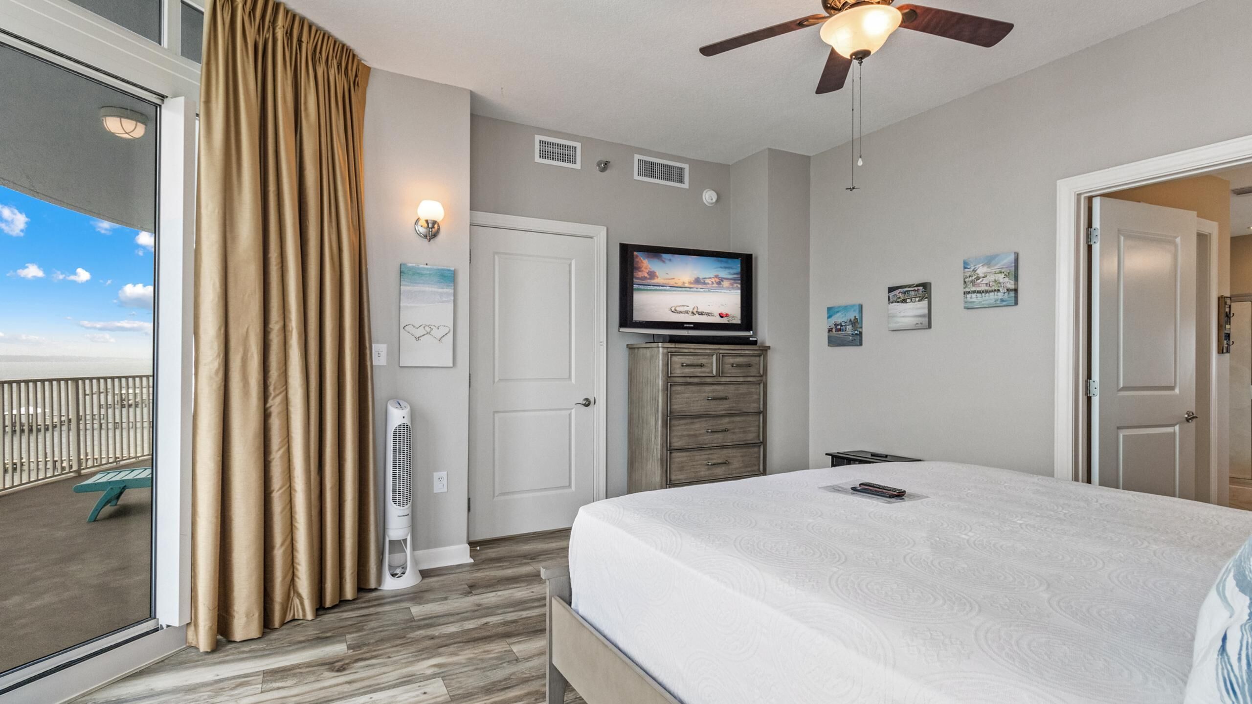 A hotel room with a bed, a television, a heater, and a view of the ocean.