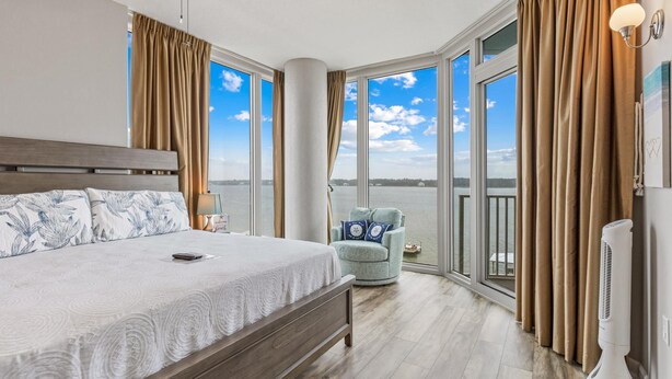 A bedroom with a large bed, a chair, and a view of the water. - Peggy's Paradise at Lagoon Tower #502 by Southern Vacation Rentals (Gulf Shores)