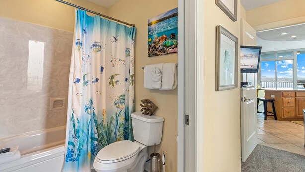 A bathroom with a shower curtain featuring marine life, a toilet, a towel rack, and a framed picture above the toilet. - Peggy's Paradise at Lagoon Tower #502 by Southern Vacation Rentals (Gulf Shores)
